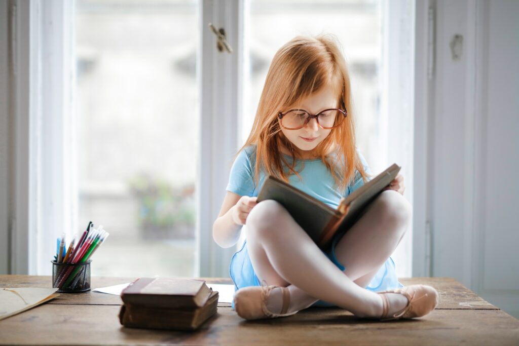 A child who understands reading is important sitting on a window sill reading a book in their lap