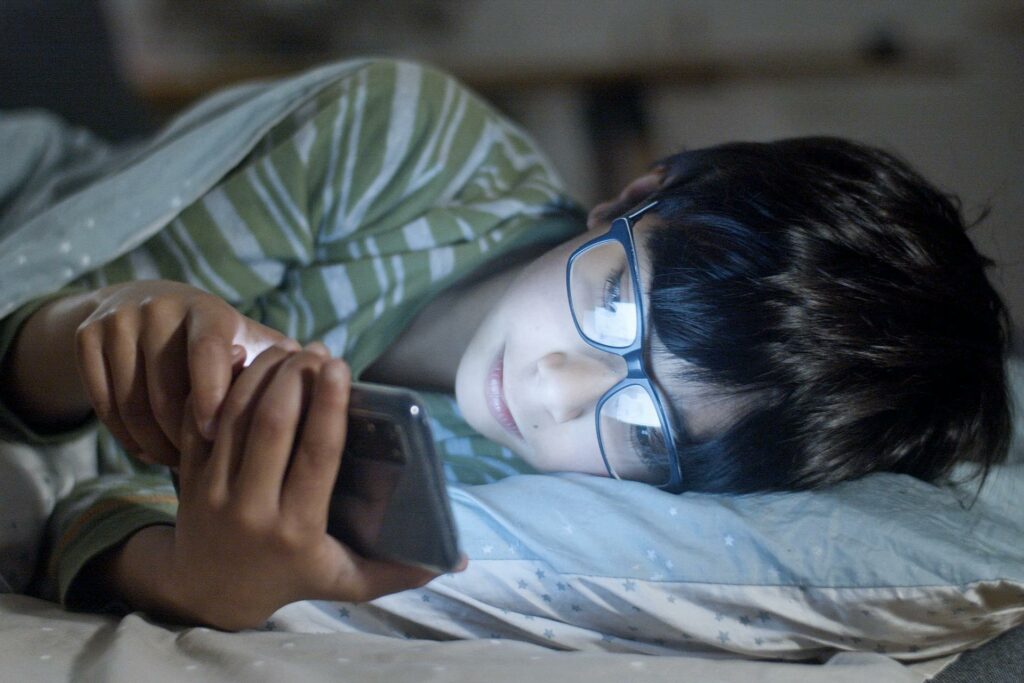 A child on a smartphone in bed, this is an example of unhealthy screen time for children